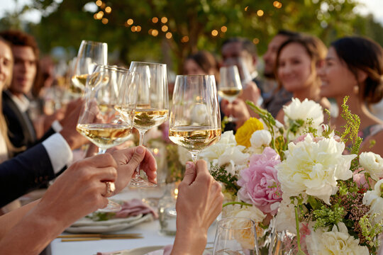 wedding guests cheering with wine glasses during toast, elegant table settings visible, floral centerpieces