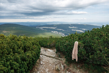 A hanging, lost by someone, beige jacket on a stone path of a tourist route passing through mountain pine trees in the Karpacz Mountains, Poland.