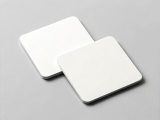 Two blank white square coasters on a gray background