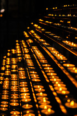 Many lit small mysterious candles lined up in a church for prayers