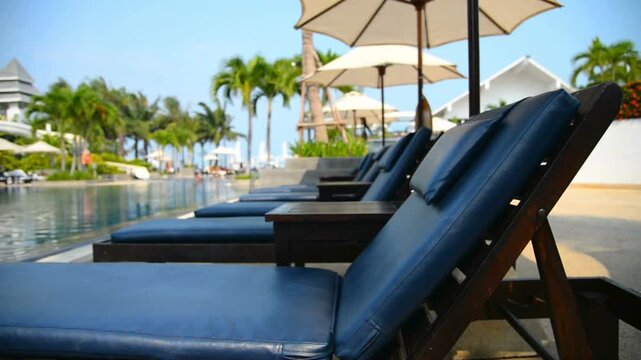 A row of lounge chairs by the pool at a tropical resort on a sunny day
