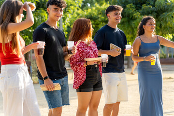Group of gen z friends eating and drinking together outdoors