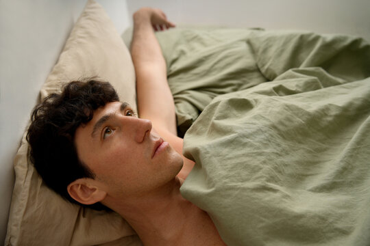 Young man lying awake in bed with morning light