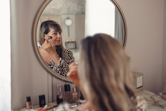 Woman applying makeup in front of round mirror