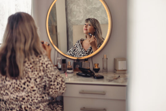 Mature woman applying make up in front of mirror