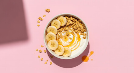 Vibrant yogurt bowl with banana, granola, and honey on pink background. A healthy, delicious breakfast or snack option.