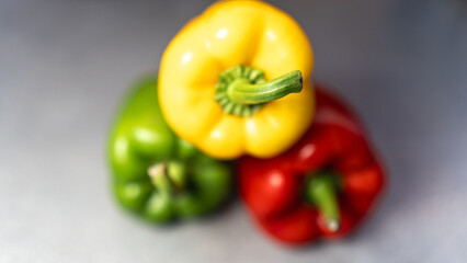 Vibrant trio of fresh whole bell peppers (yellow, green, red) on a rustic countertop. Perfect for healthy food ads, recipe books, and market visuals.