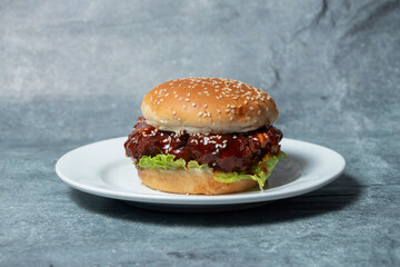 Korean Fried Chicken Burger with Lettuce and Tangy Sauce on Sesame Bun in plate side view of junk food