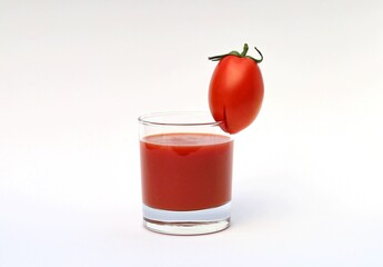 A glass of tomato juice. With a small tomato on the edge.