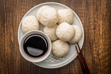 Xiao long bao. Chinese dumplings and soy sauce on plate on wooden table. Top view.