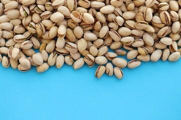 Tasty unpeeled pistachios on bright blue background, top view flat lay background pattern