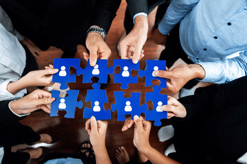 Diverse professionals collaboratively holding blue puzzle pieces that symbolize networking, connection, and partnership in a corporate environment, demonstrating teamwork and unity. Amity