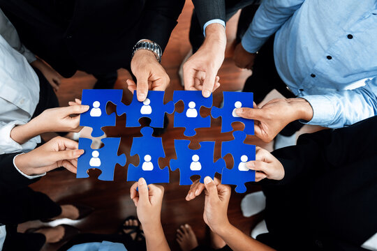 Diverse professionals collaboratively holding blue puzzle pieces that symbolize networking, connection, and partnership in a corporate environment, demonstrating teamwork and unity. Amity