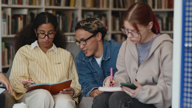 Stab shot of Asian gen Z boy helping his biracial female classmate with university assignment studying together in comfortable modern library among peers