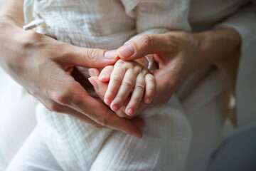 Baby's hand lies on mother's hands, close-up