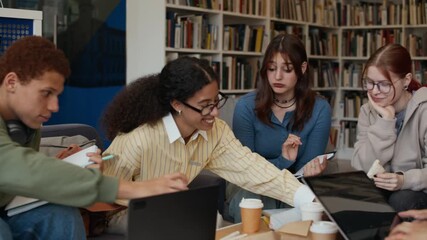 Pan shot of young diverse group of motivated students sitting in university library and working on assignments together - Powered by Adobe
