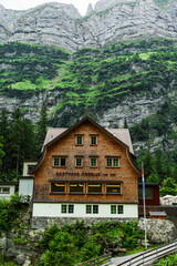 Obraz premium Traditional Swiss mountain guesthouse Berggasthaus Seealpsee surrounded by lush alpine forest and steep rocky cliffs in the Appenzell Alps, Switzerland.