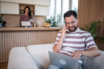 Freelancer working from home, talking on phone and using laptop