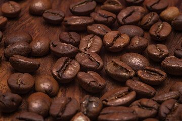 Close-up of roasted coffee beans scattered on a wooden background. Highlighting their rich brown color and textured surface. Inviting coffee lovers to indulge. Selective focus.