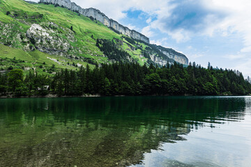 Fototapeta premium Tranquil Seealpsee lake reflecting lush green meadows and towering alpine peaks in the Swiss Alps, creating a breathtaking summer mountain landscape.