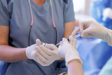 Nurse drawing medication from vial with syringe in hospital close view