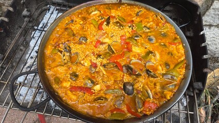 Traditional spanish paella with seafood and vegetables on outdoor grill. Typical cuisine of Spain. Valencian cuisine. Stage of cooking paella. Ingredients for paella