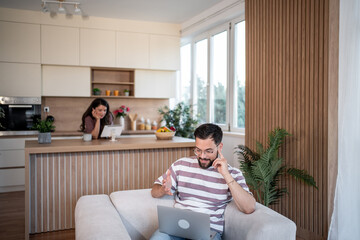 Man working from home having video call while woman using tablet in kitchen