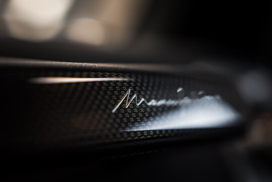 Close up view of a glossy carbon fiber interior detail featuring the Mansory logo. The texture and craftsmanship are highlighted against a blurred background.