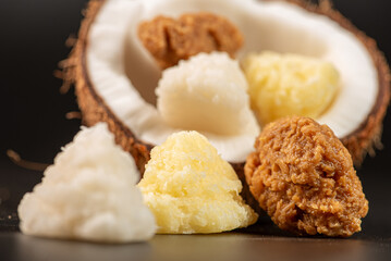 Open coconut and coconut sweets (cocadas) placed on a dark surface, black background, selective focus.