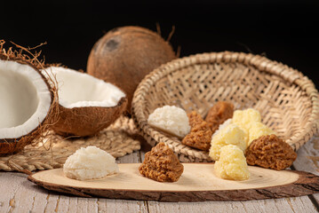 Open coconut and coconut sweets (cocadas) placed on a rustic wooden surface, selective focus.