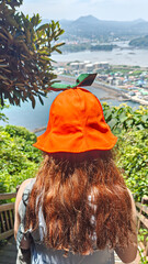Closeup view of a woman wearing a popular Jeju Island tangerine ribbon bucket hat looking down from from Seongsan Ilchulbong volcano to Seogwipo