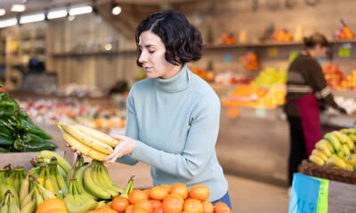Female shopper carefully selects fresh bananas and other fruits in a grocery supermarket