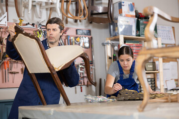 Male and female carpenters working on restoring vintage mirror and chair in workshop