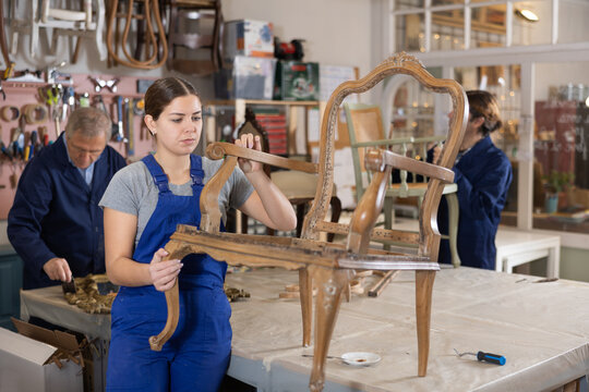 Professional craftswoman restorer in uniform renewing old-fashioned chair while working in repair shop