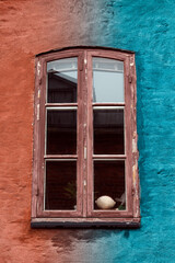 Fototapeta premium Beautiful Old Window with Blue and Red Wall Colors. A charming old window set in a weathered wall featuring striking blue and red colors.