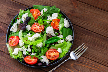 Fresh green salad with tomatoes and cheese served on a wooden table