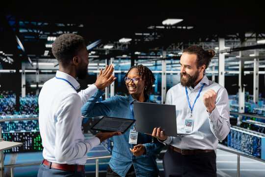 Multiethnic confident team sharing a high five to celebrate achievement on server farm industrial platform, cheering to their professional collaboration. Pleased successful engineering team. - Powered by Adobe