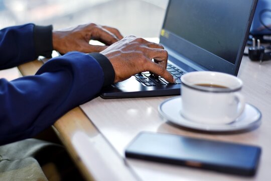 Hands typing on laptop at work desk, cup of coffee beside