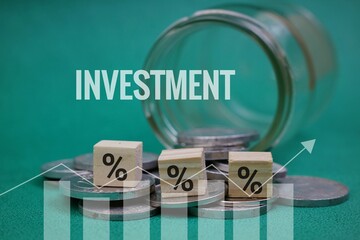 A pile of coins spilling out of a glass jar with a percentage symbol on a wooden block and a graph. Investment concept. Isolated on a green background.