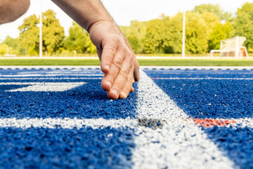 Athlete preparing to start sprint on blue running track, hand positioned on the ground, showcasing determination and focus before the race begins