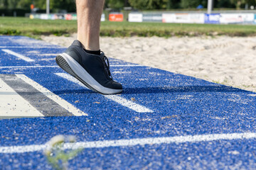 Athlete prepares for long jump with foot poised on blue runway, showcasing athletic footwear and textured surface in a competitive environment