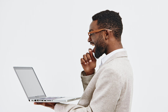 Young smiling African American man wearing glasses and beige sweater using a laptop computer in profile view isolated on white background. People lifestyle concept. - Powered by Adobe