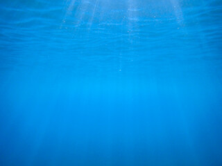 Ocean blue underwater with sunrays, Underwater Sea Deep Water Abstract Sunshine, sea wave , clean waters in summer time, Natural underwater seascape, sand on ocean floor and water surface with sunligh