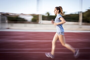 Obraz premium A woman is actively running on a track during a bright day, capturing speed.