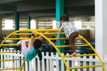 Naklejka premium Portrait of sister and brother playing on the playground together. Happy little child climbing on outdoor monkey bars. Kindergarten preschool. Children summer activities. Rear back view.