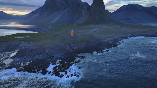 Drone captures a black sand beach, calm waters, and a towering mountain in Iceland at sunset, with gentle waves and smooth transitions in motion.
