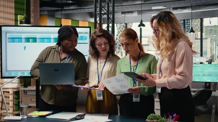 Multiethnic women form a powerful team discuss business strategy, analyzing performance data on laptop and documents aligned around success, progress and shared objectives. Camera A. - Powered by Adobe
