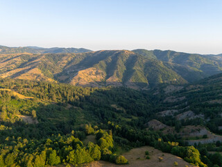 Obraz premium Aerial drone view of a lush forested mountainous landscape in Turkey with sunlit hills and dense greenery, showcasing the rich natural environment and serene beauty of the countryside.