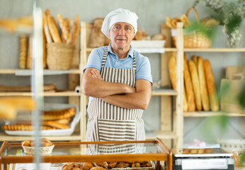 Mature man seller in uniform while working in bakery