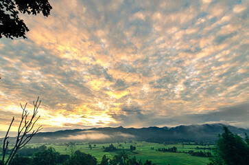 Beautiful sunrise view, sunlight hitting altocumulus clouds on mountain tops and misty rice fields, Chiang Rai, Thailand, is the beauty of the rainy season.